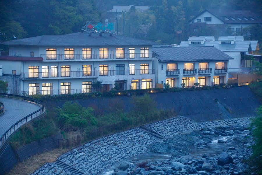 Nakagawa Onsen Shingenkan with this scene, where its long riverside facade overlooks fast-moving water at dusk.
