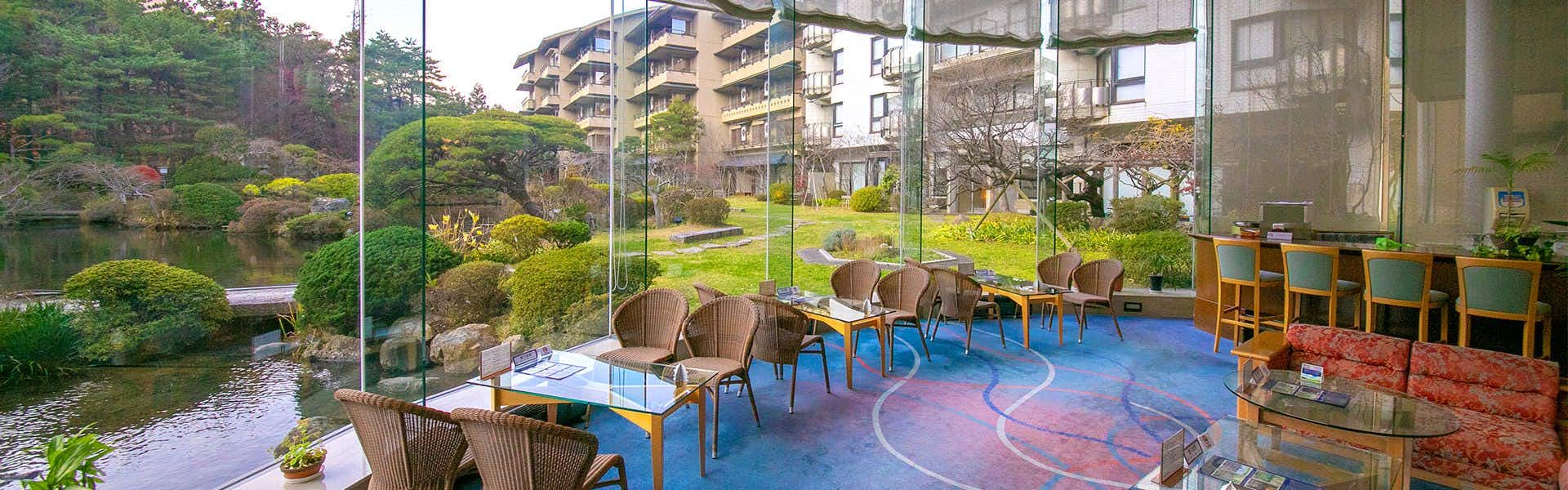 Shikisai Ichiriki Interior floor with blue tiled sections and red tiled sections, woven seating chairs, glass wall opening to exterior garden and multi-level building structure.