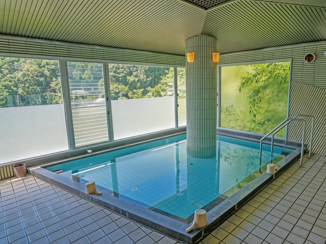A tiled indoor bath with a central column and broad windows overlooking trees.