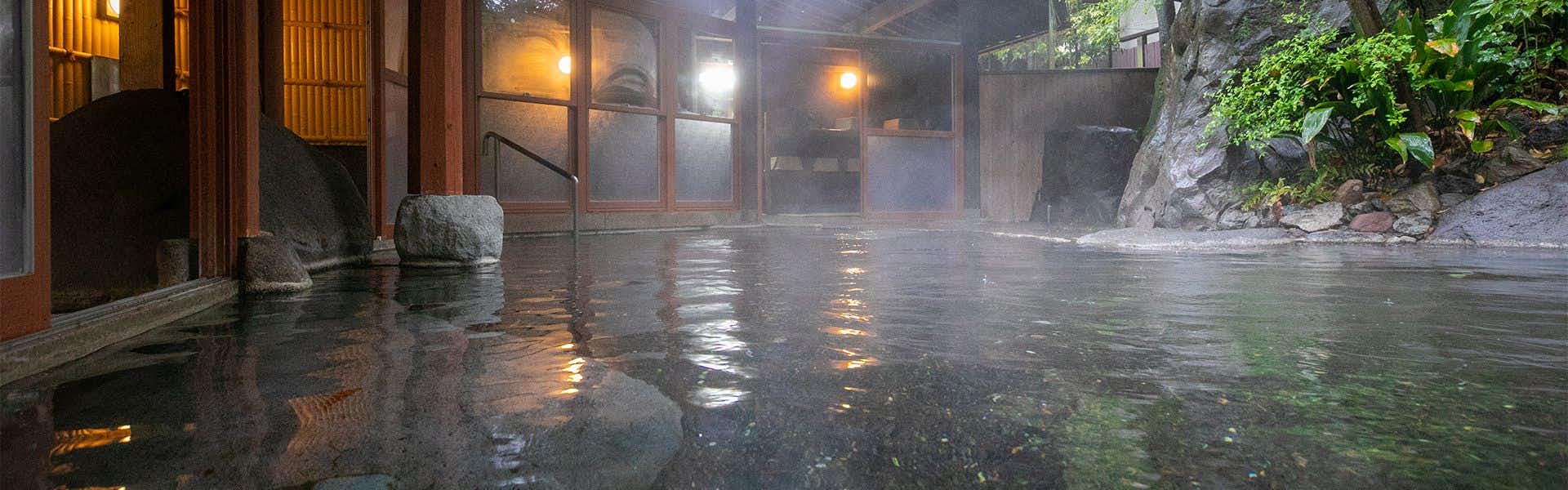 Yufuin Onsen Hinoharu Ryokan with an open-air stone bath beside timber fencing and garden plants.