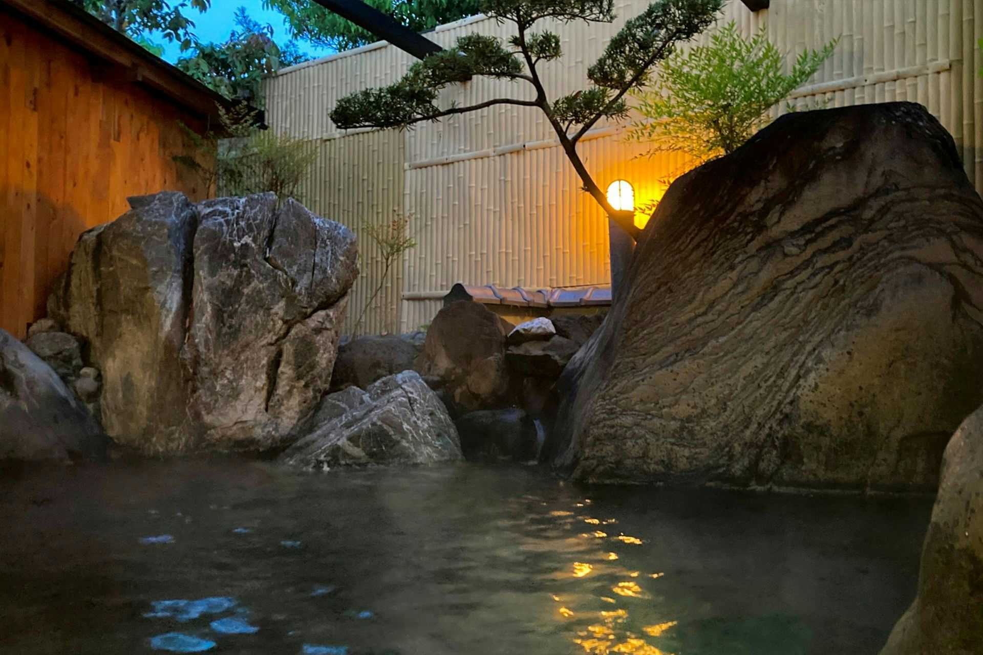 Ueki Onsen Ryokan Kirinoyu with this scene, where a rock-lined open-air bath sits behind a timber wall and garden planting.