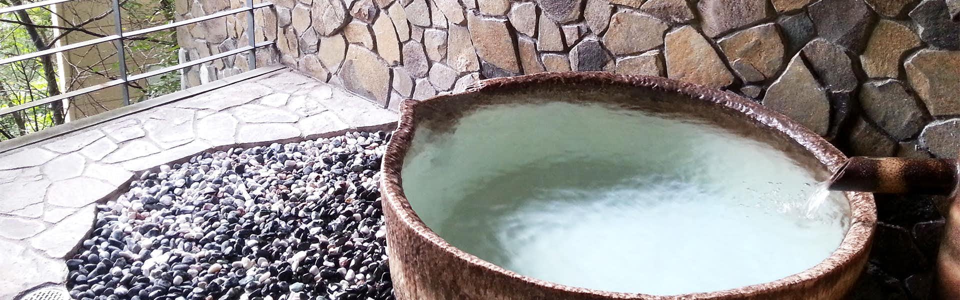 Kawafuru Onsen Yamagatakan round ceramic bath beside a stone wall and dark pebbles