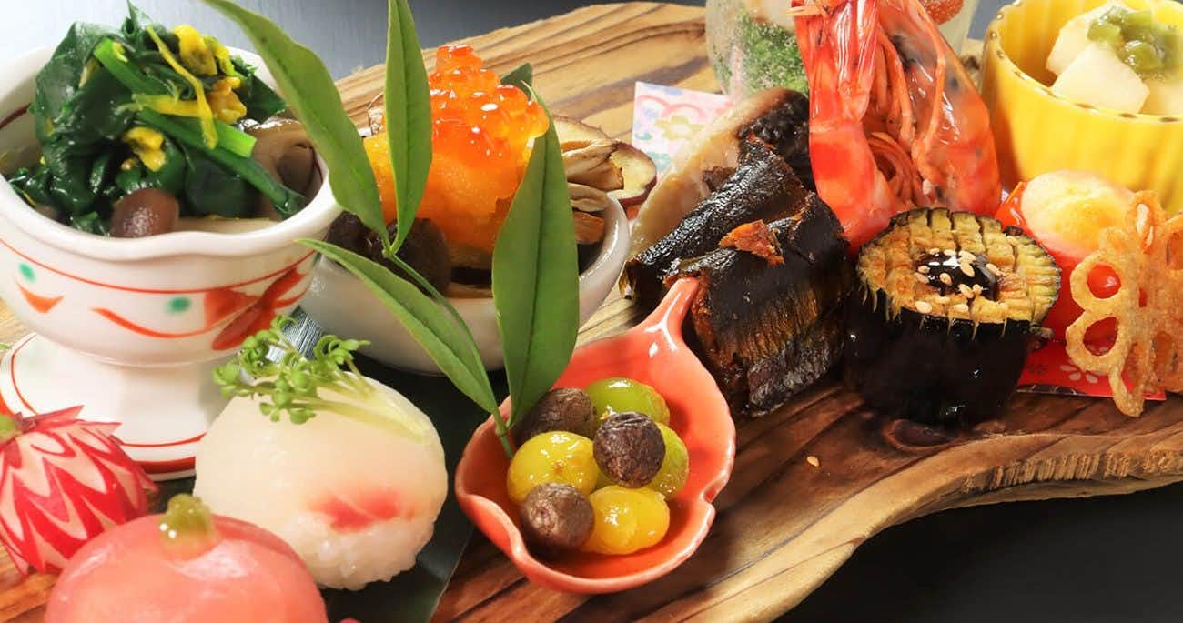 Oyado Yunosato assorted prepared items in ceramic bowls and red dishes on wooden board, with fresh green stems as garnish.