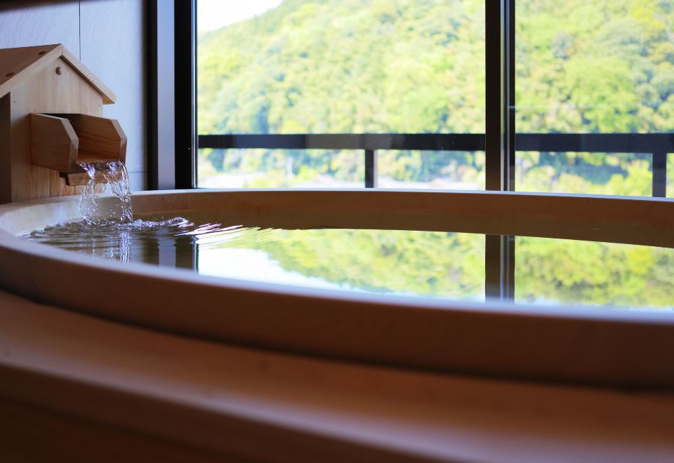 Water flowing into a wooden bath beside a window.