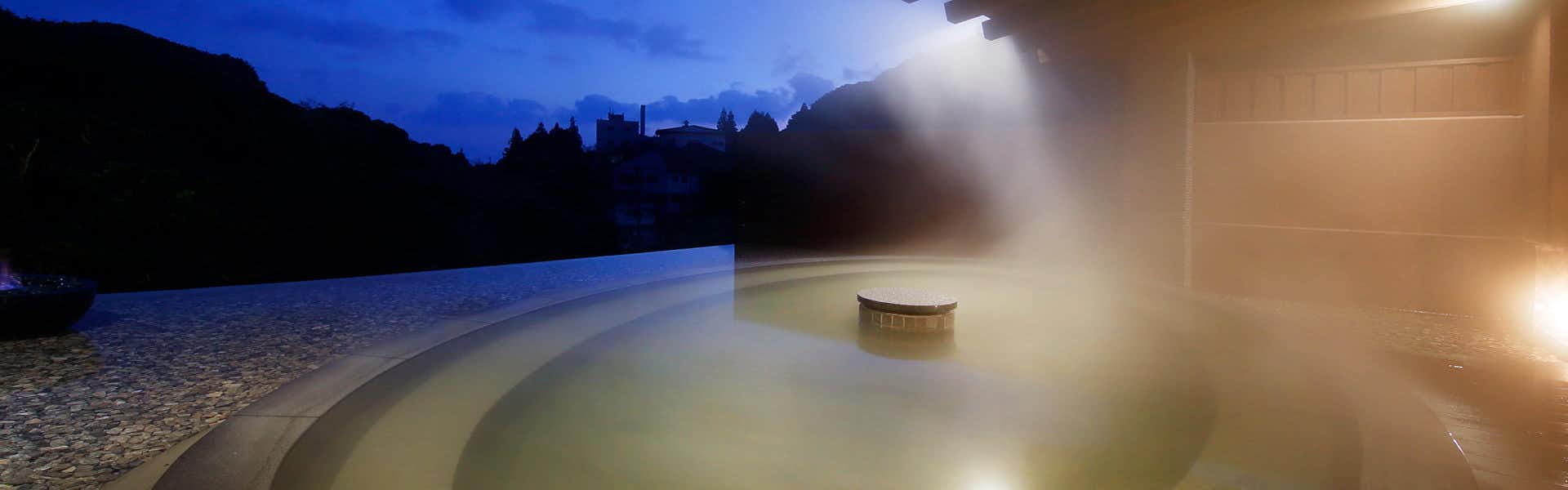 Unzen Onsen UnzenFukudaya with a steaming outdoor bath overlooking dark mountain silhouettes.