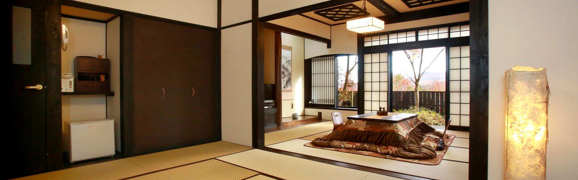 Minami Aso Onsen Iyashi no Sato Hatago Seiwa Tatami guest room with low covered table, floor chair, garden windows, dark timber trim, refrigerator, and floor lamp