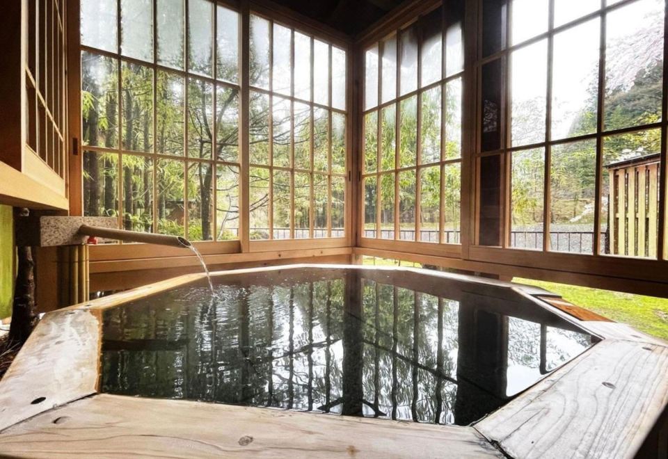 A bath with a wooden rim beside tall windows facing trees.