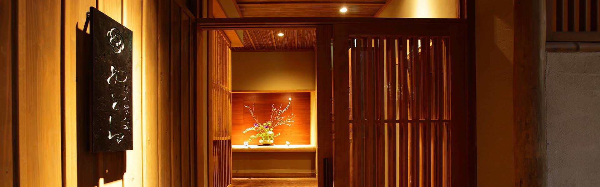 Kyokoyado Yutone Illuminated wooden signage with Japanese characters at entrance, surrounded by vertical wooden lattice doors and warm interior lighting.