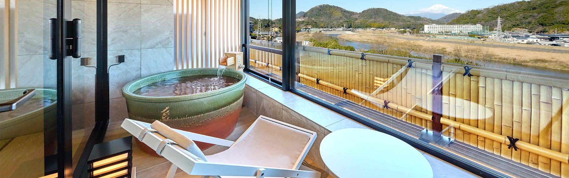 Fugaku Hanabusa Circular green bathtub with water visible through large windows overlooking mountains and valley, with modern black fixtures.