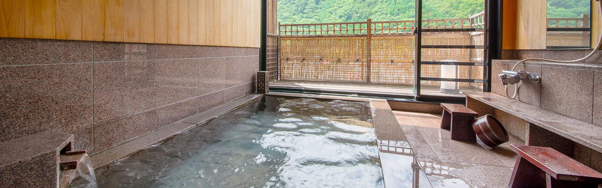 Yamamizuki URARA Tsutaya with a stone-lined indoor bath opening toward a mountain-view balcony.