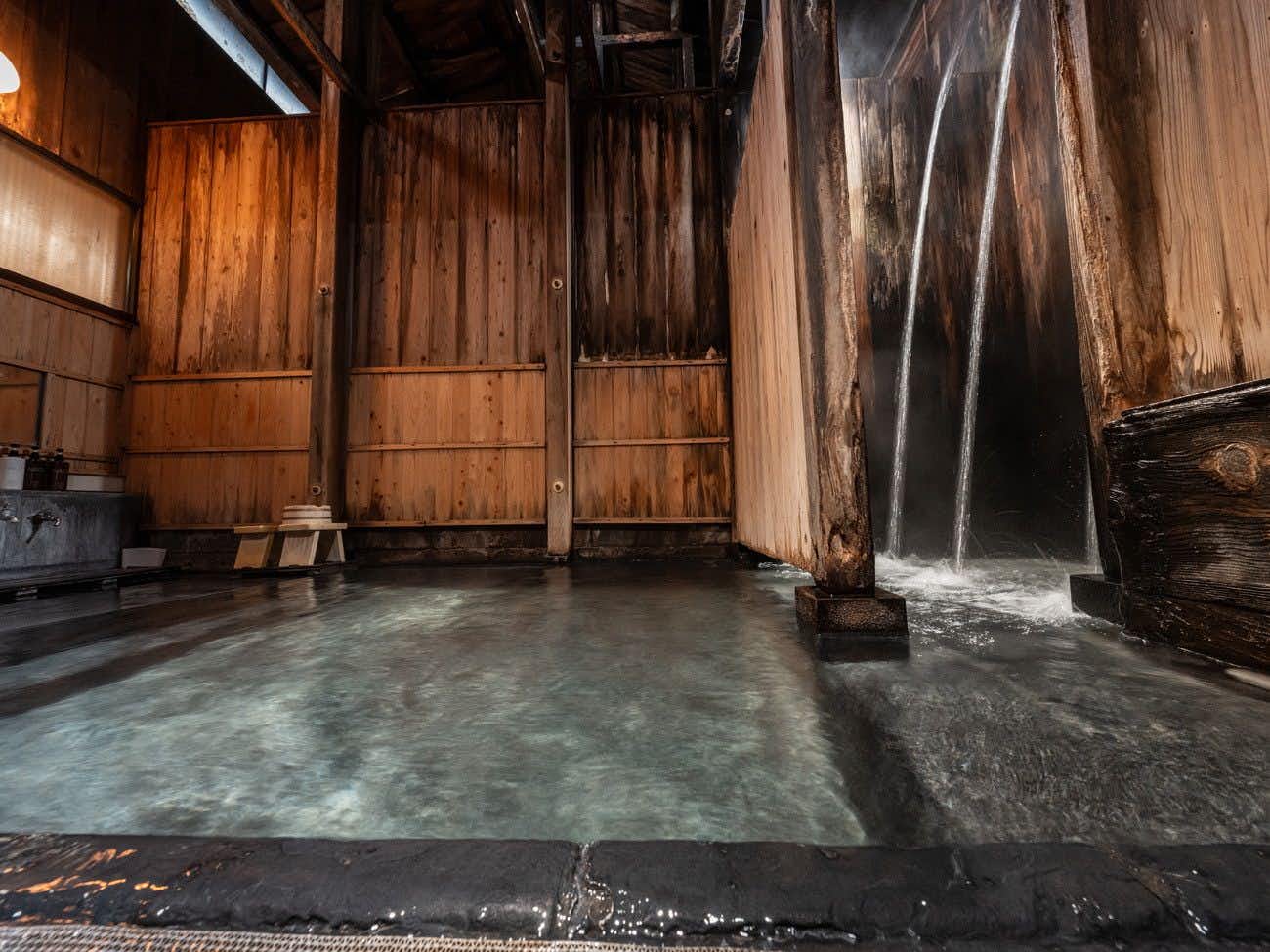 Shirabu Onsen Higashiya tall wood-walled indoor bath with a cascading wall spout