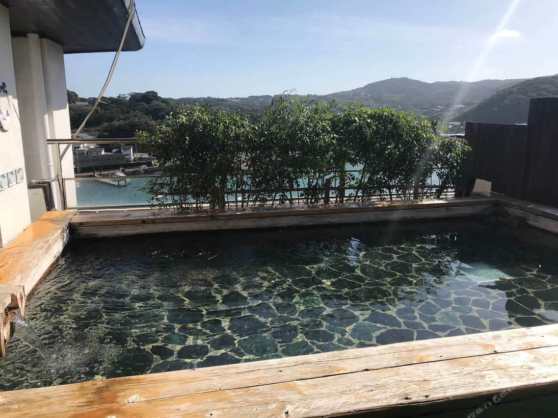An outdoor bath behind a hedge with hills in the distance.