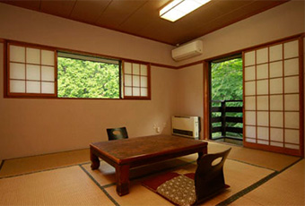 A tatami room with a low table and windows facing trees.