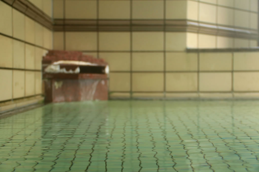 A tiled indoor bath is filled beside a traditional water spout.