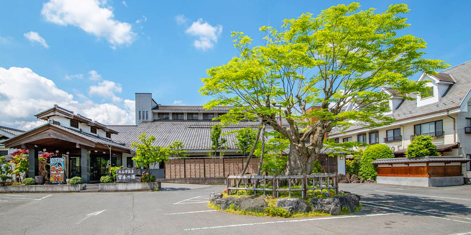 Its traditional entrance, landscaped forecourt, and leafy summer trees.