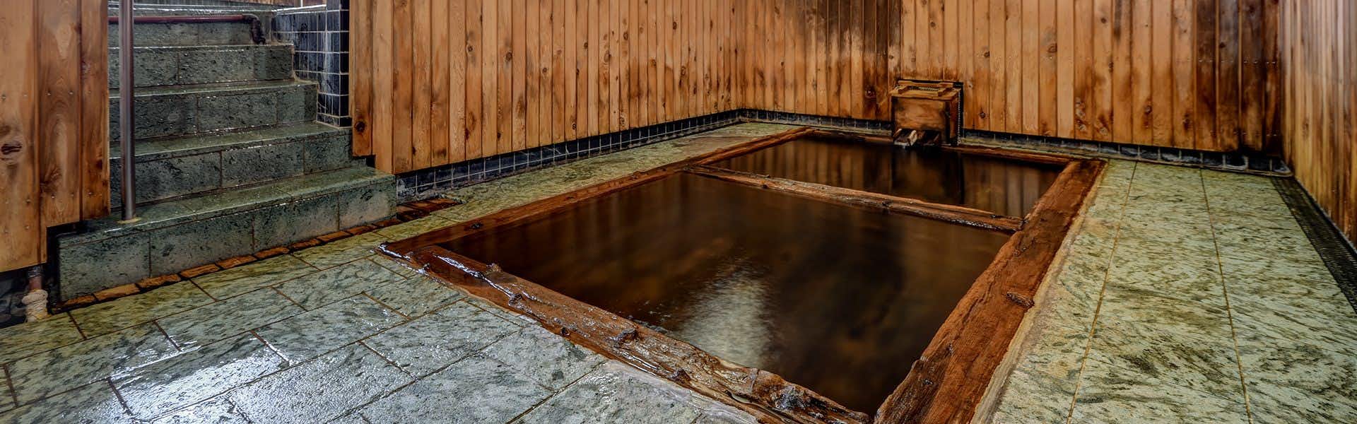 Tsugaru Clan Honjin Inn Yanagi no Yu with a rectangular wooden bath surrounded by gray stone flooring.