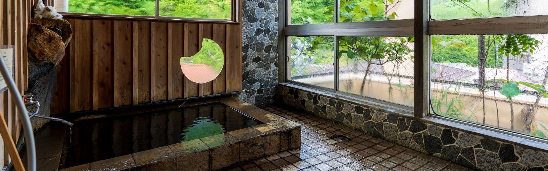 Ryokan Oonuma Stone-lined bathing pool beside broad windows with forest greenery visible outside