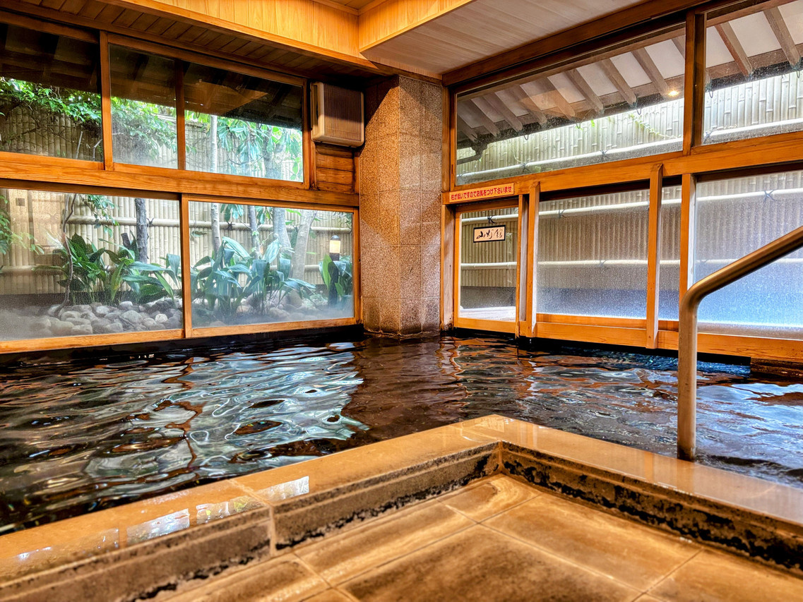An indoor bath beside large wooden-framed windows.