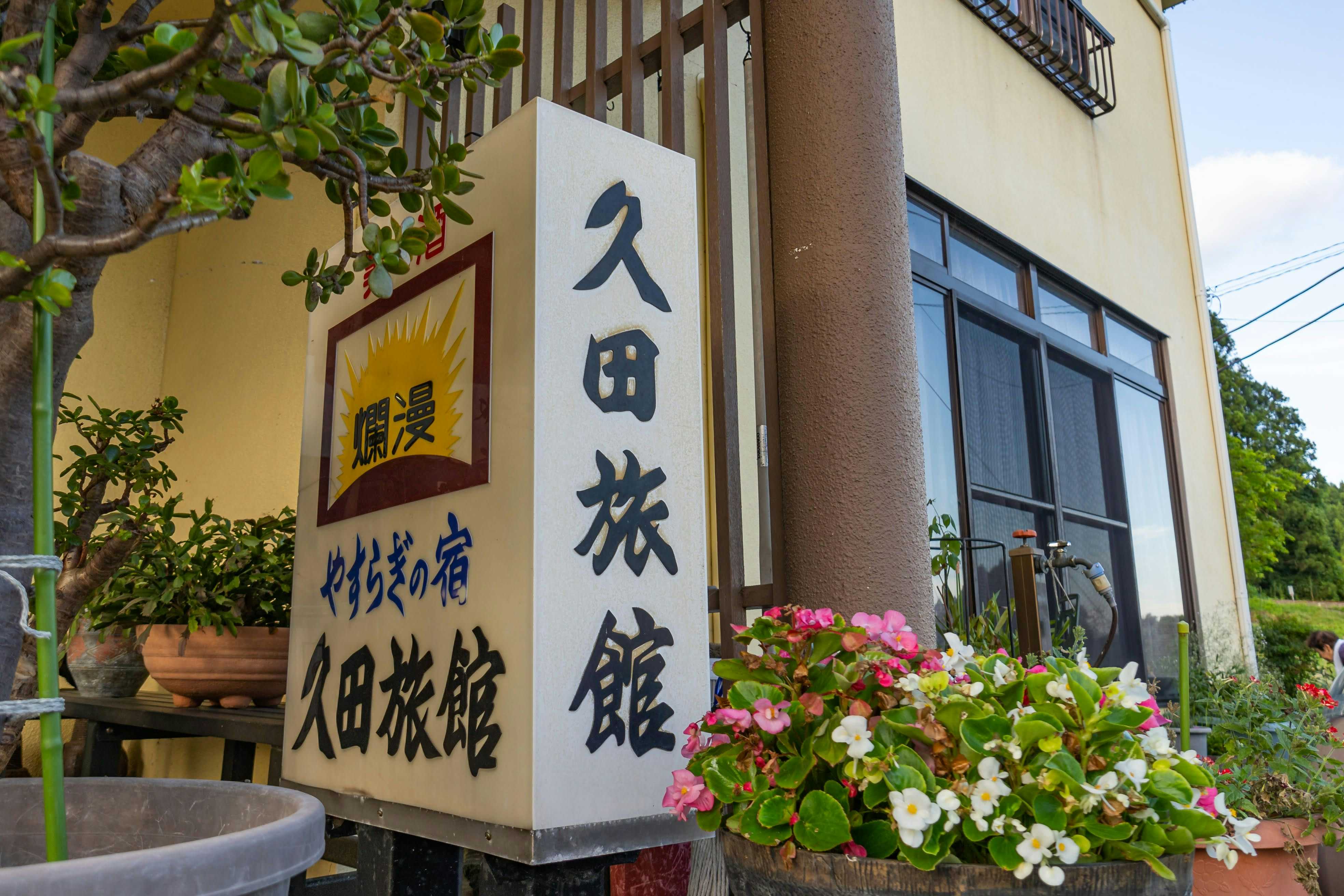 Kyuden Ryokan with the vertical property sign beside flowering garden plants.