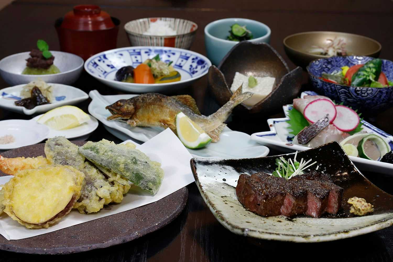 Yufuin Onsen Onyado Nakaya with seasonal tempura and grilled fish arranged across ceramic dishes.