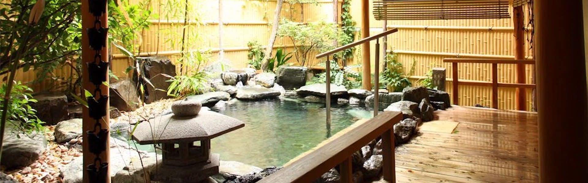 Hotel Kameya Honten with an open-air garden bath beside rocks and bamboo fencing.
