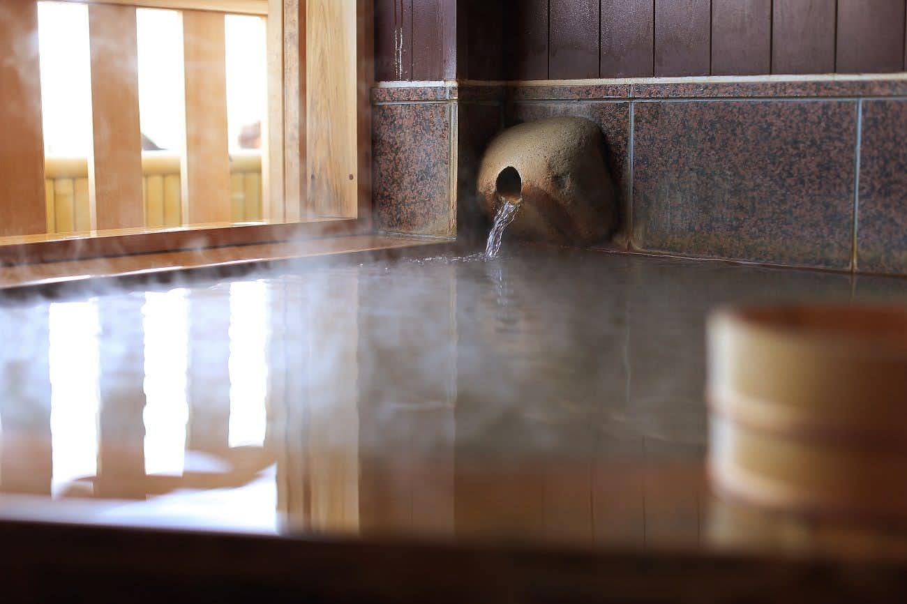 Chiaki Jinsentei Close view of clear water flowing from a rounded stone spout into a steaming tiled bath beside a wooden window