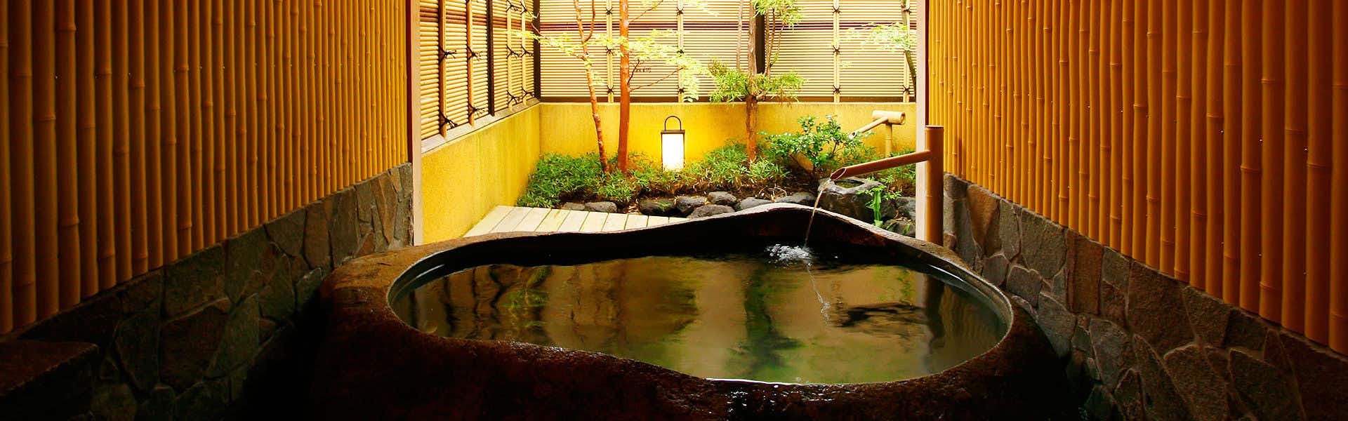 Nishi-Izu Toi Yagisawaso with this scene, where a dark stone bath sits beside a planted courtyard and warm timber screening.