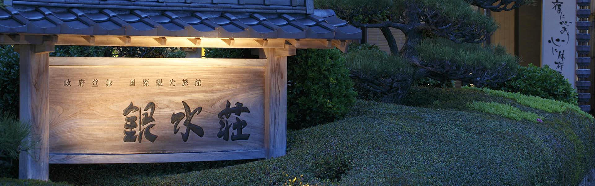 The stone property sign glowing beside a dark garden.