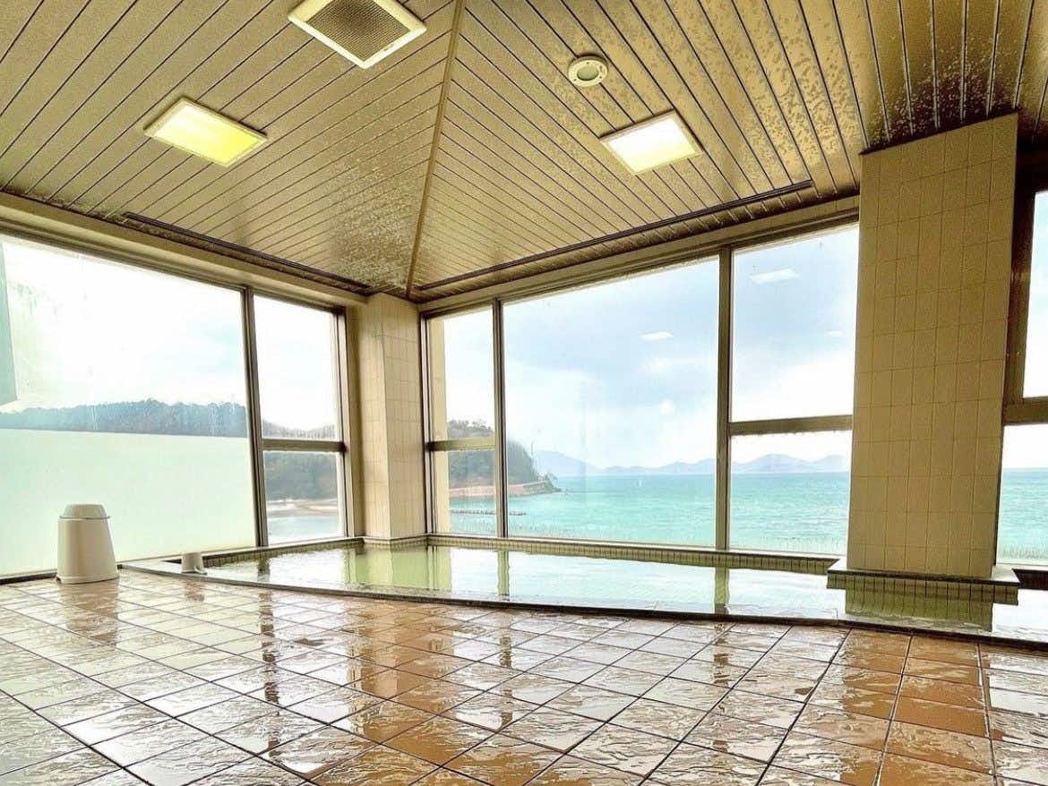 Shikisai no Yado Hanatsubaki with an indoor tiled bath overlooking turquoise coastal water.