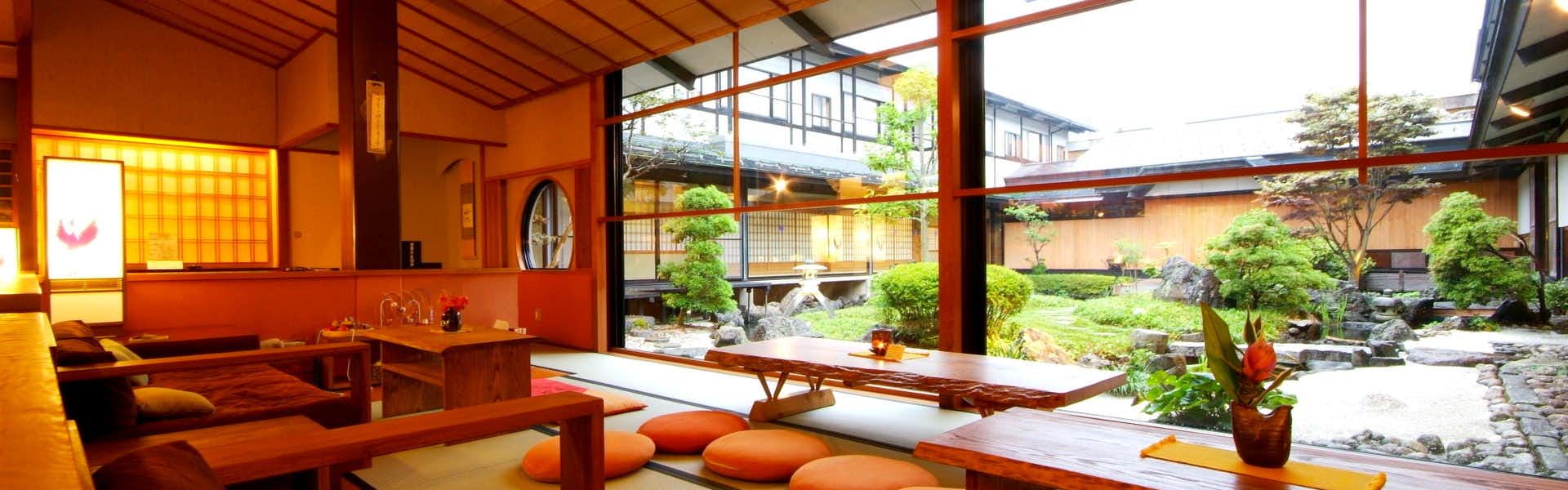 Kinosaki Onsen Onishiya Suishoen Room interior with wooden beams, red seating, and garden view through windows.