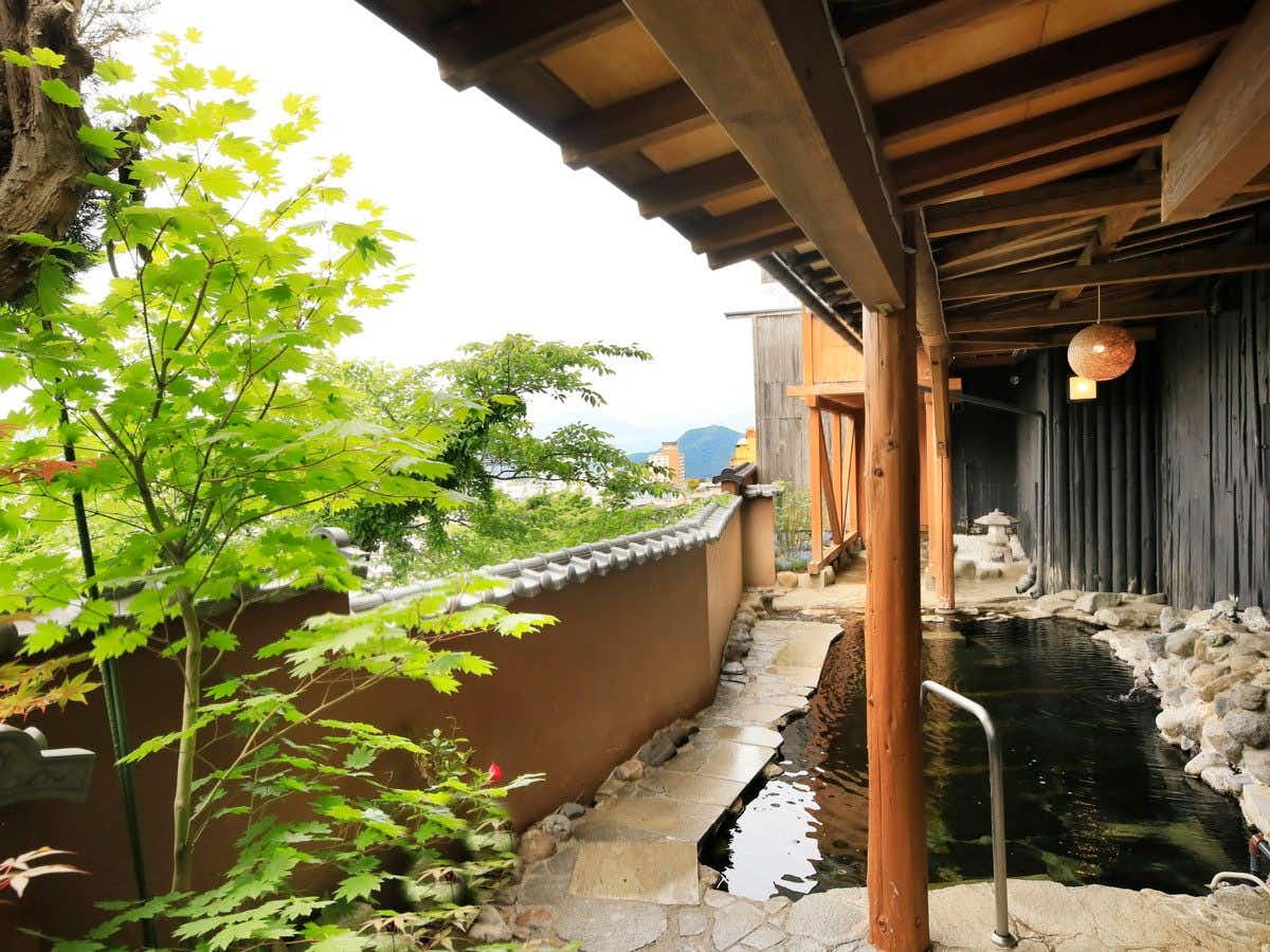 Ryokan BIYUNOYADO with a narrow garden waterway beneath fresh green leaves.