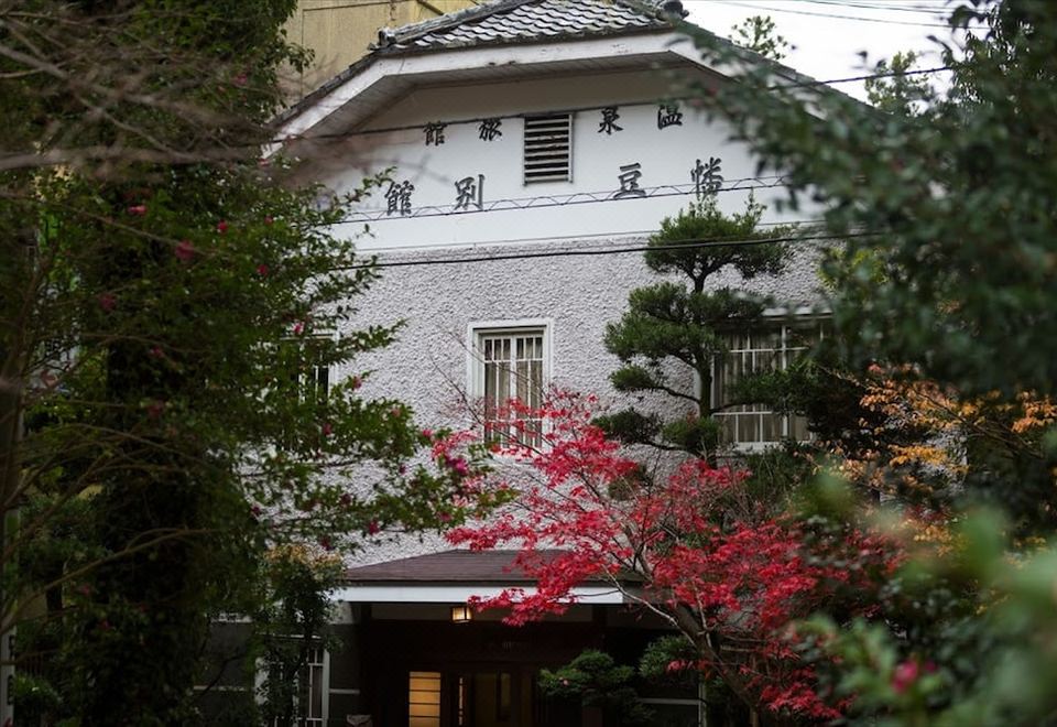 White traditional facade partly screened by red blossoms and trees.