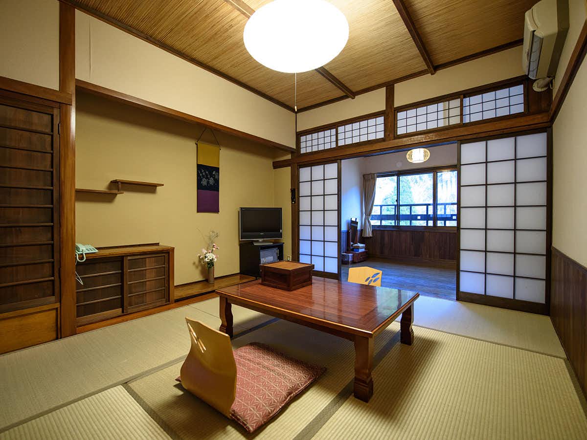 Yunohira Onsen Ryokan Kamiyanagiya Tatami room with a polished low table, floor chairs, shoji panels, warm wood trim, and an adjoining window alcove.