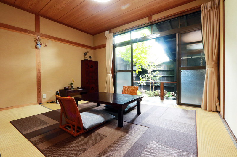 A traditional tatami room has a low dark table, two floor chairs, and a bright garden-facing window.