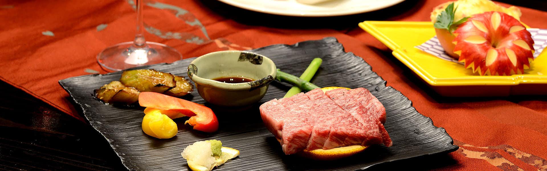 Oyado Hanamizuki with grilled beef and colorful appetizers arranged on black stone.