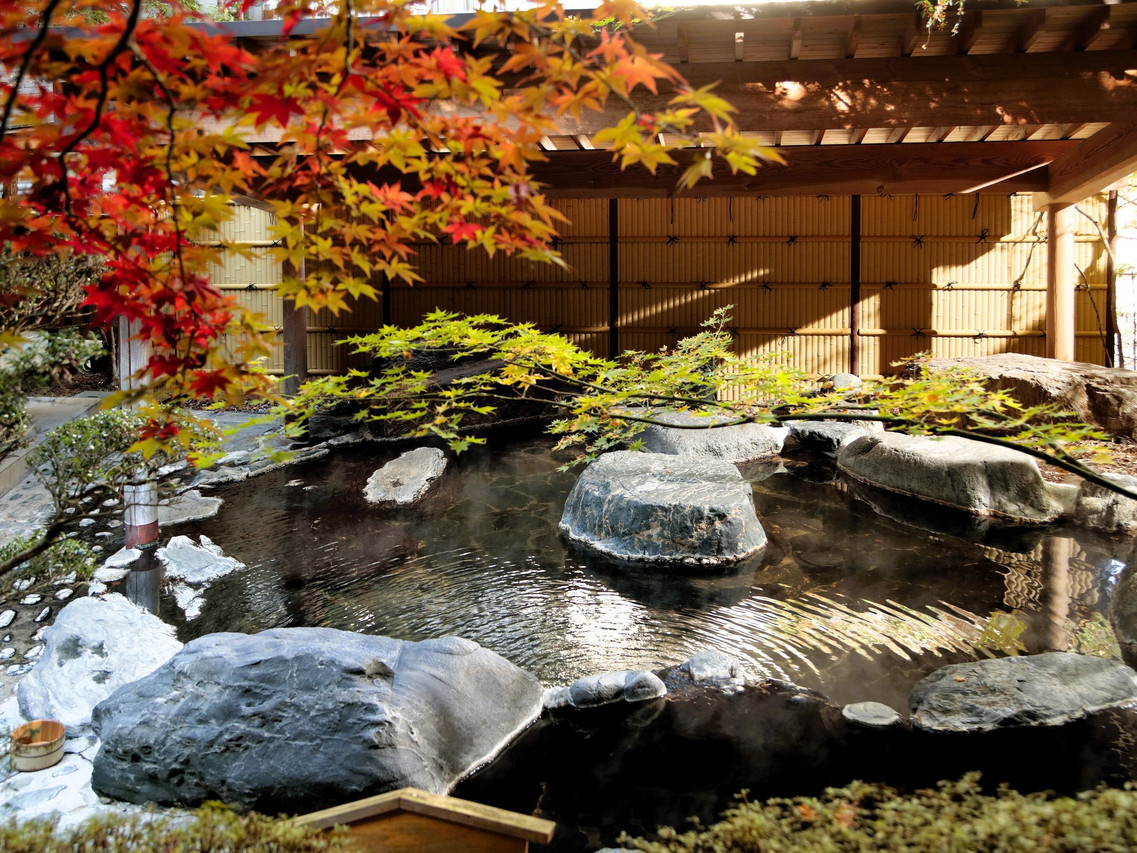 A stone-lined outdoor pool sits beneath red autumn foliage.
