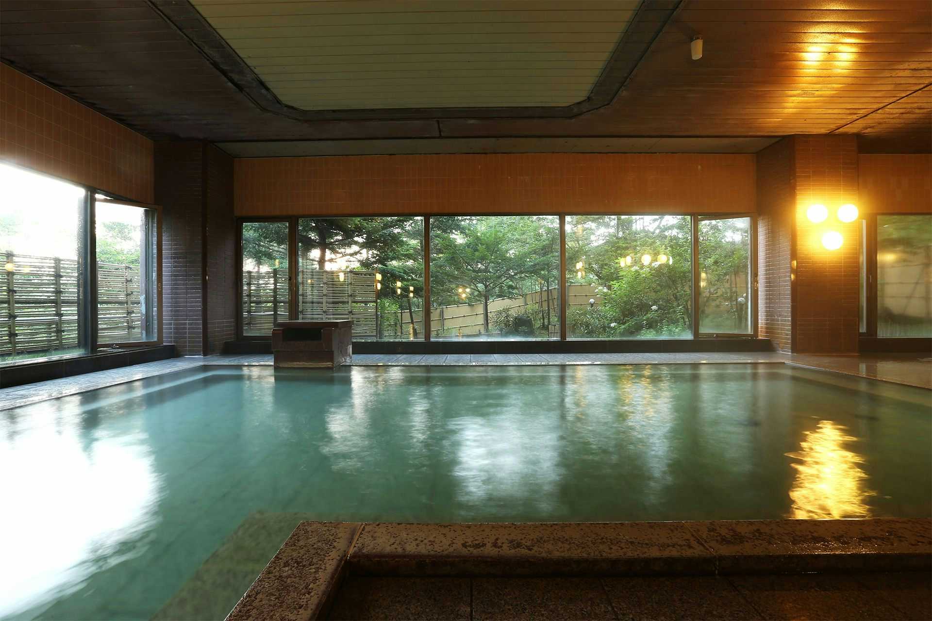 Kusatsu Onsen Hotel Sakurai with a spacious indoor bath reflecting garden trees through broad windows.