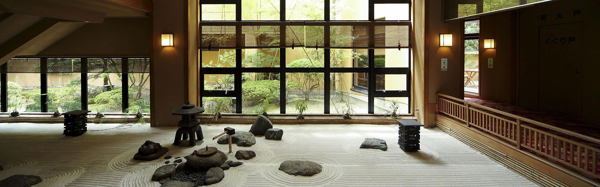Tabist Chikuba Shinyotei Hakodate Yunokawa Onsen Interior garden space with large window wall, gravel grounds, stone arrangement, and greenery beyond glass.
