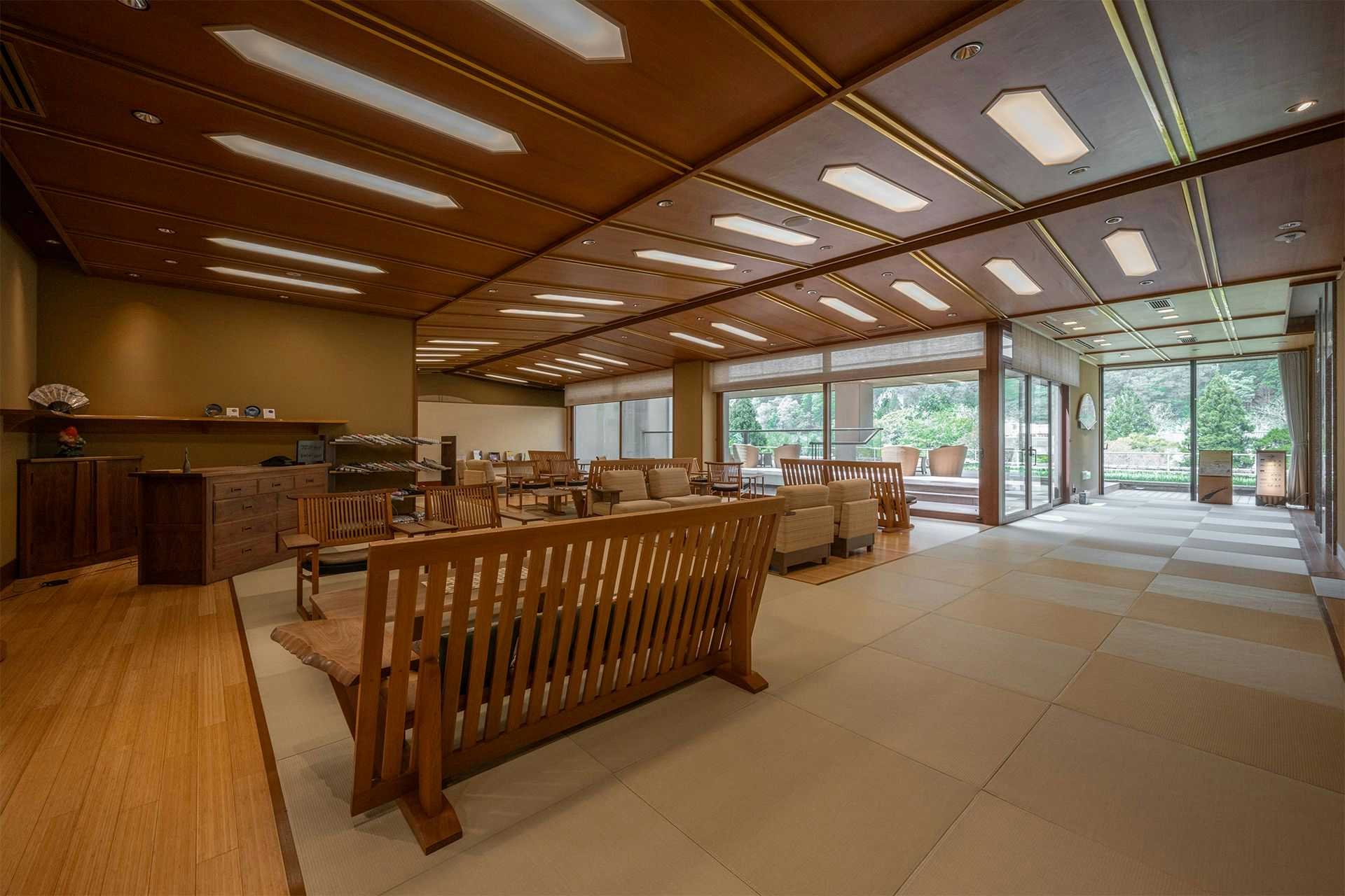 Kuriya Yasohachi Large wood-toned lounge with rows of benches and chairs, broad windows, open terrace, and geometric ceiling lights