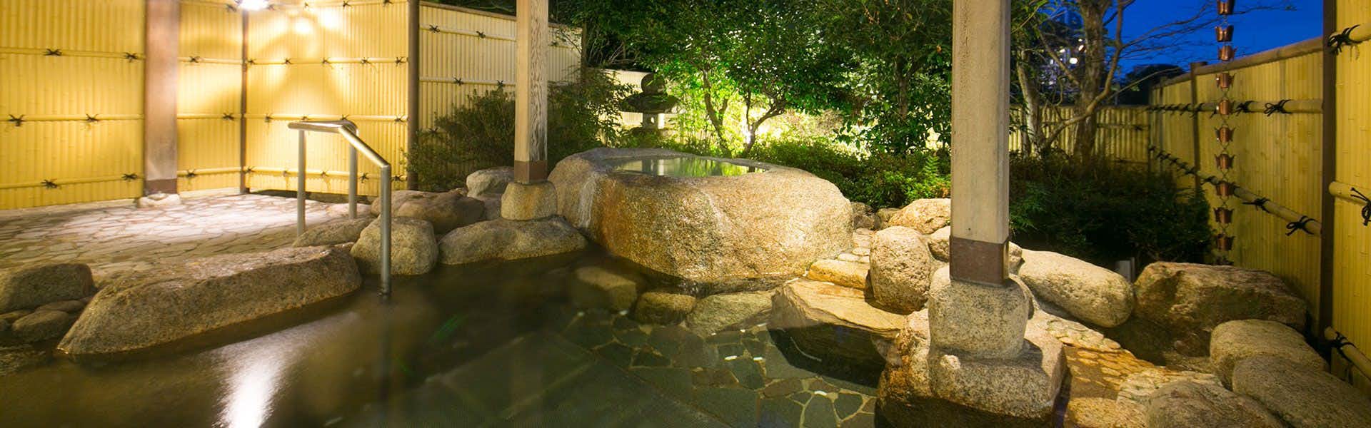 Shikanoyu Hotel with an open-air rock bath surrounded by leafy garden plants.