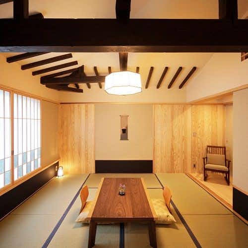 A minimalist tatami room beneath exposed dark rafters.