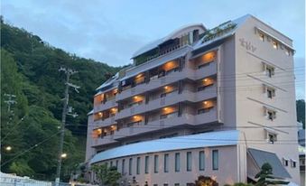 Multi-storey ryokan exterior at dusk against a wooded hillside.