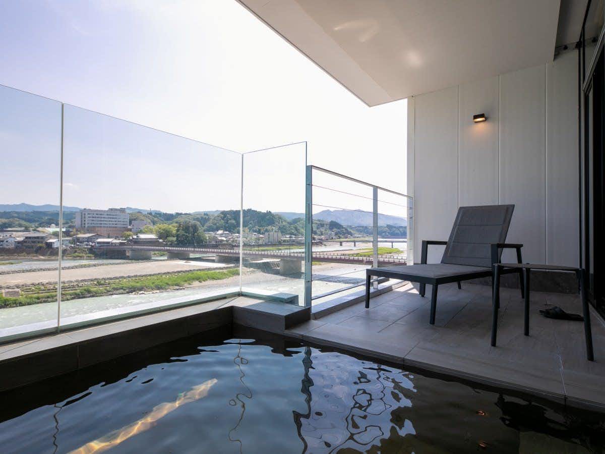 Hitoyoshi Onsen Nabeya (Formerly: Nabeya Main Building) with an open-air bath overlooking the river and distant hills.
