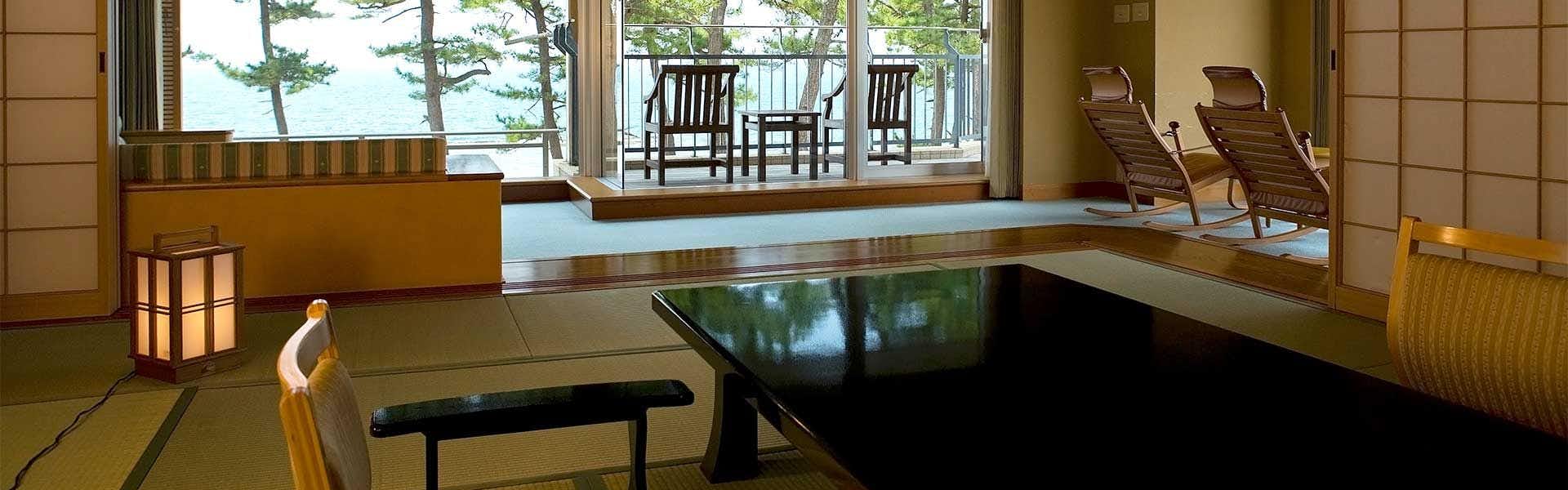 Kasuitei Interior with sunken lounge seating around glossy dark table before wide coastal windows, exposed timber ceiling, light wood surfaces