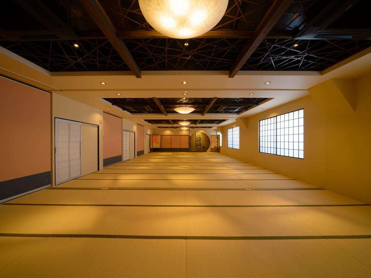 Ryokan Kouro with an expansive tatami hall beneath dark timber ceiling beams.