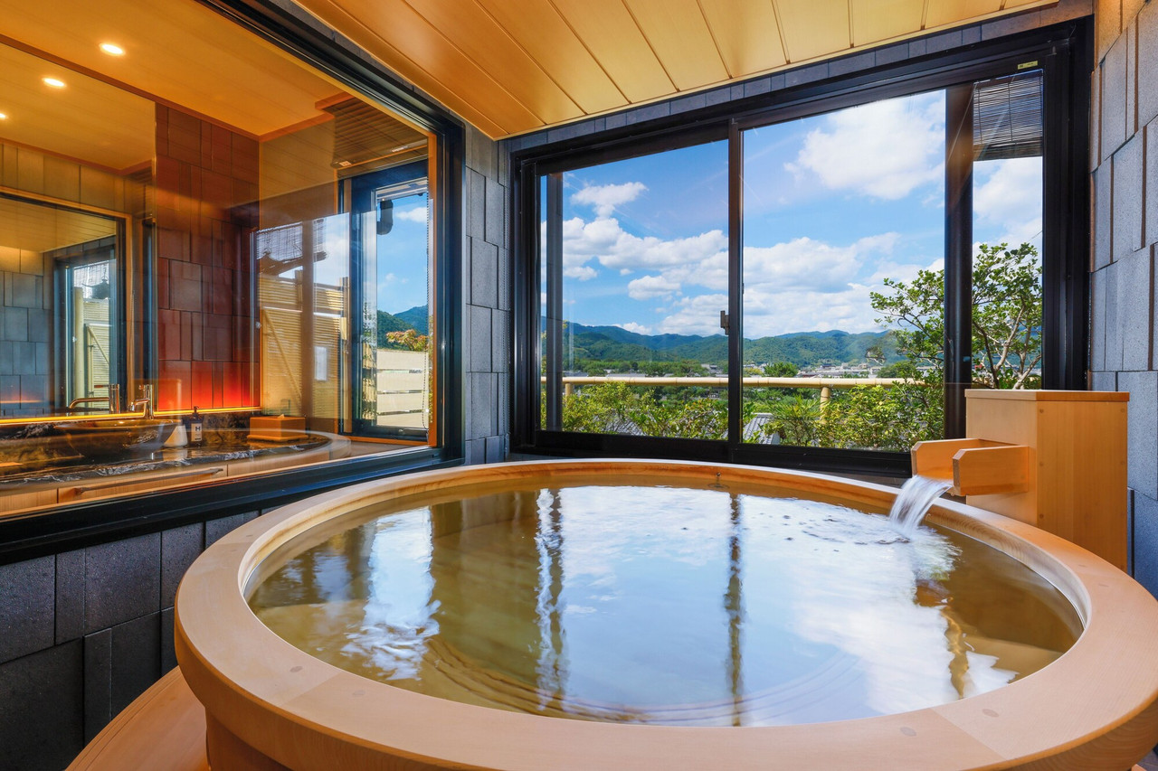 A round wooden bath beside broad windows overlooking hills.