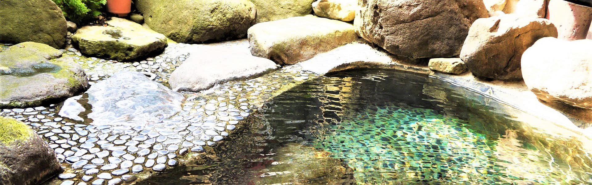 Aizu Higashiyama Onsen Irori no Yado Ashina with an outdoor bath amid smooth rocks.