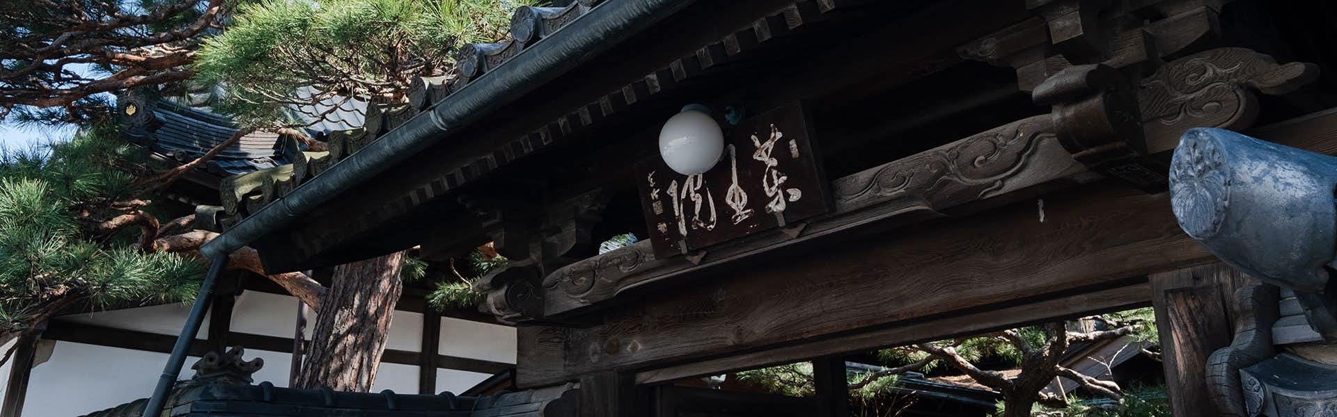 Shinshu Zenkoji Yakuoin with carved timber exterior eaves framed by evergreen branches.
