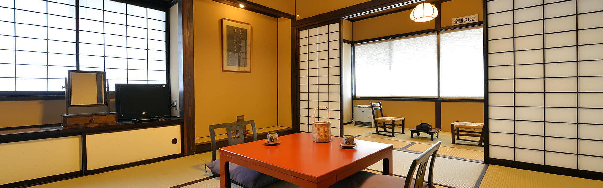 Ryokan Sugimoto wide tatami room with a red low table, television and shoji windows