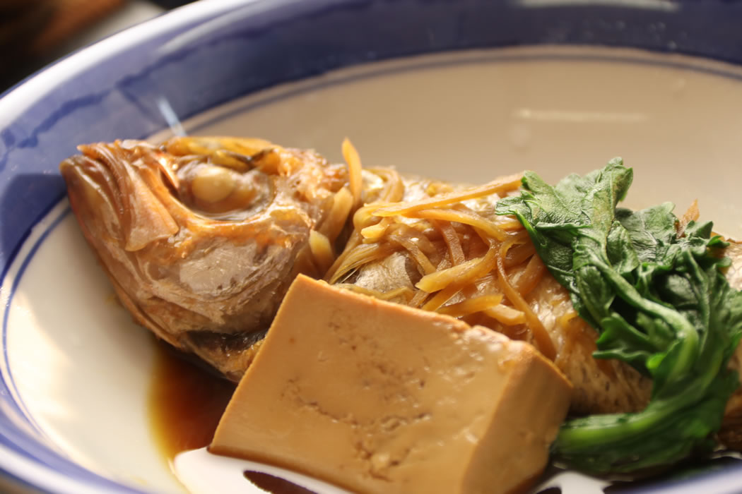 A simmered fish is plated with tofu and leafy greens.